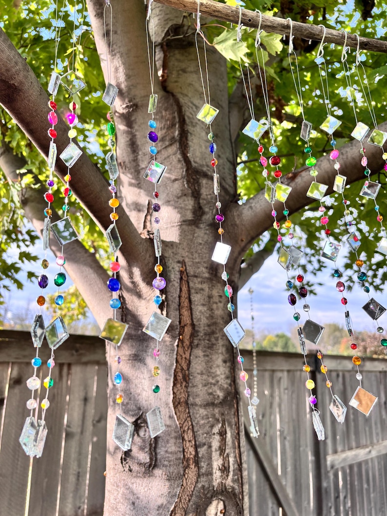 Puede incluir: Cadenas decorativas colgantes con cuentas de colores y detalles de espejo cuadrados. Las cadenas est&aacute;n suspendidas de una rama de &aacute;rbol, creando una vibrante exhibici&oacute;n de color y luz. Las cuentas son de varios colores.