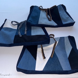 May include: Three denim fabric bags with geometric patchwork designs in shades of blue, white, and black. Each bag has a drawstring closure with a brown cord. The bags are arranged on a white surface.
