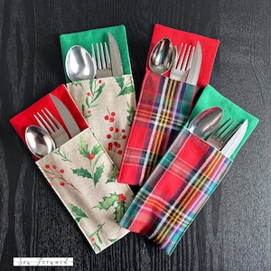 Może przedstawiać: Kolekcja świątecznych etui na sztućce. Etui mają różne wzory, w tym wzory ostrokrzewu i jagód oraz czerwono-zieloną kratę. Każde etui zawiera widelec, nóż i łyżkę ze stali nierdzewnej, idealne na świąteczne spotkania.