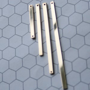 May include: Four gold-colored metal bars with holes at each end. The bars are arranged in a fan shape, with the shortest bar at the top and the longest bar at the bottom.