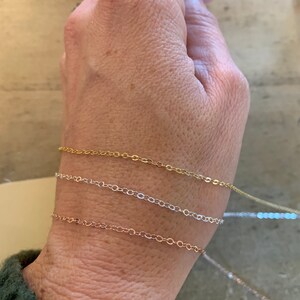 Peut inclure: Quatre bracelets d&eacute;licats en cha&icirc;ne dor&eacute;e, argent&eacute;e et or rose. Les bracelets sont superpos&eacute;s au poignet d'une personne.