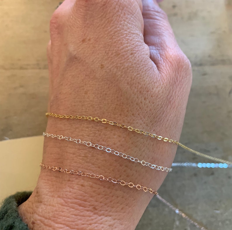 Peut inclure: Quatre bracelets d&eacute;licats en cha&icirc;ne dor&eacute;e, argent&eacute;e et or rose. Les bracelets sont superpos&eacute;s au poignet d'une personne.