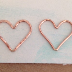 May include: Two copper-colored heart-shaped pendants. One has a hammered texture, the other is smooth. The hearts are displayed on a light blue and white background. These pendants are suitable for jewelry making.