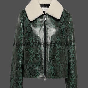 May include: A long-sleeve jacket featuring a green and black snakeskin pattern, a white faux fur collar, and a central black zipper closure. The garment includes two front patch pockets and a white interior label with the text SignatureHideCo.