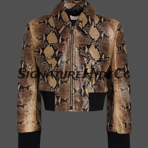 May include: A cropped jacket featuring a brown and black snakeskin pattern, a pointed collar, a central silver zipper, two chest pockets with flaps, and solid black ribbed knit cuffs and a matching black ribbed hemline. The text SIGNATUREHYDECO is visible.