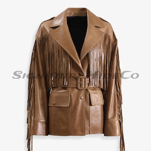 Può includere: Giacca in pelle marrone con frange sulle maniche e sul petto. La giacca ha una cintura in vita, due tasche anteriori e un colletto. La giacca è di colore marrone medio.