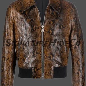 May include: A brown and black snakeskin-patterned jacket with a full-length silver zipper, a pointed collar, and black ribbed cuffs and hem. The text SIGNATURE HIDE CO is printed across the chest area of the jacket in a dark, semi-transparent font.