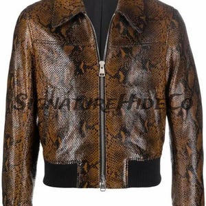Könnte beinhalten: Braune und schwarze Jacke mit Schlangenmuster, schwarzem Kragen, Bündchen und Saum. Die Jacke hat einen Reißverschluss und den Text "SIGNATURE HIDE CO" auf der Vorderseite. Die Jacke ist im Bomber-Stil.