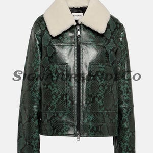 Może przedstawiać: Zielona kurtka ze wzorem skóry węża z kremowym kołnierzem z kożucha. Kurtka ma zamek błyskawiczny, dwie przednie kieszenie i logo na kołnierzu. Stylowa odzież wierzchnia.