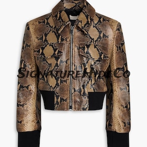 Pode incluir: Casaco castanho e bege com padrão de pele de cobra, gola, punhos e bainha pretos. O casaco tem fecho de correr e dois bolsos frontais. O texto "SIGNATURE TRADE CO" é visível no casaco.