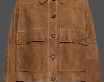 May include: A brown suede jacket featuring a classic collar, long sleeves, and a front button closure with five dark buttons. The garment includes two large rectangular chest pockets with horizontal flaps and visible stitching throughout the design.