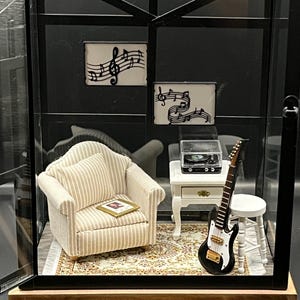 May include: Miniature diorama featuring a living room scene with a striped armchair, a small table with a record player, and a black and white guitar. The walls display musical notes. The scene is enclosed in a glass case.