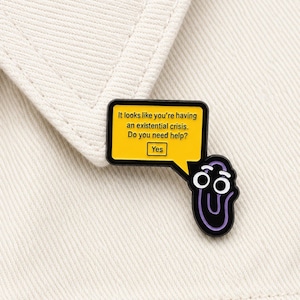 May include: A novelty enamel pin in black and purple, shaped like a paperclip with a speech bubble. The yellow speech bubble has the text: "It looks like you're having an existential crisis. Do you need help? Yes."