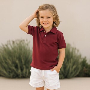 Pode incluir: Uma crian&ccedil;a vestindo uma camisa polo bord&ocirc; com gola e shorts brancos. Os shorts t&ecirc;m cintura com cord&atilde;o. A crian&ccedil;a est&aacute; sorrindo e com a m&atilde;o no cabelo.