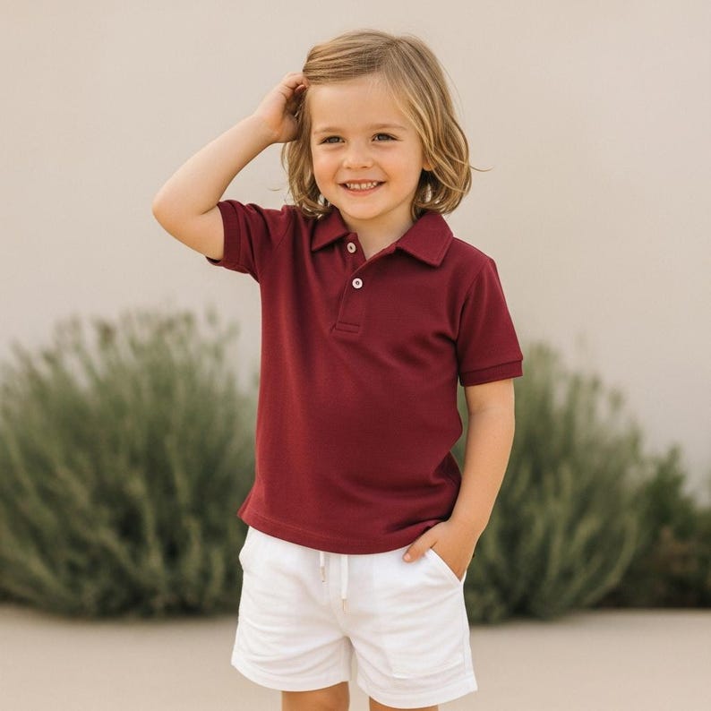 Pode incluir: Uma crian&ccedil;a vestindo uma camisa polo bord&ocirc; com gola e shorts brancos. Os shorts t&ecirc;m cintura com cord&atilde;o. A crian&ccedil;a est&aacute; sorrindo e com a m&atilde;o no cabelo.