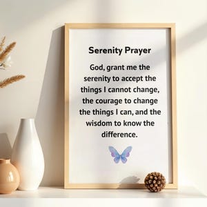 Peut inclure: Impression encadrée avec la Prière de la Sérénité, un papillon à l'aquarelle et un cadre en bois clair. L'impression est exposée sur une étagère blanche avec des vases décoratifs et une pomme de pin.