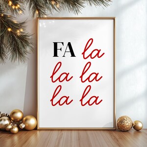 Può includere: Una stampa incorniciata con le parole "FA la la la la la la" in corsivo nero e rosso. La stampa è in una cornice dorata ed è esposta su una superficie di legno con ornamenti dorati e verde.