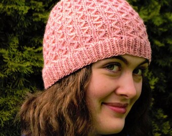 May include: A knitted pink hat with a textured diamond pattern. The hat is made of soft yarn and has a ribbed brim. The hat is a warm accessory for cold weather.