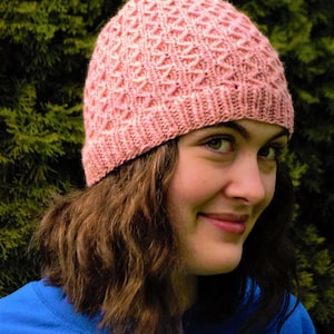 May include: A knitted pink hat with a textured diamond pattern. The hat is made of soft yarn and has a ribbed brim. The hat is a warm accessory for cold weather.