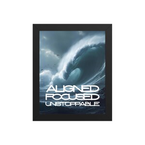 May include: Framed print featuring a dramatic ocean wave under a cloudy sky. The words "ALIGNED FOCUSED UNSTOPPABLE" are displayed in white block letters across the bottom of the image. The frame is black.