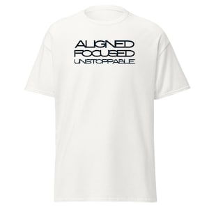 May include: A white t-shirt with the words "ALIGNED FOCUSED UNSTOPPABLE" printed in navy blue. The text is stacked vertically, with each word on a separate line. The shirt has short sleeves and a crew neck.