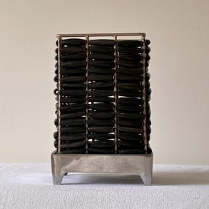May include: A rectangular decorative object featuring a silver-toned metal frame with four vertical sections. Each section is filled with stacked, dark brown, horizontally oriented, smooth, oblong beads held in place by thin metal rods.