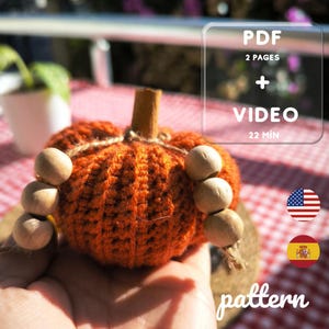 Puede incluir: Una calabaza naranja tejida a ganchillo con un tallo de canela y cuentas de madera. La imagen incluye el texto "PDF 2 pages + VIDEO 22 MIN" y la palabra "pattern".