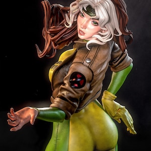 May include: A detailed figurine of a female character in a green and yellow bodysuit, brown leather jacket, and gloves. The character has brown and white hair, green eyes, and a green headband. The jacket features a red and black emblem.