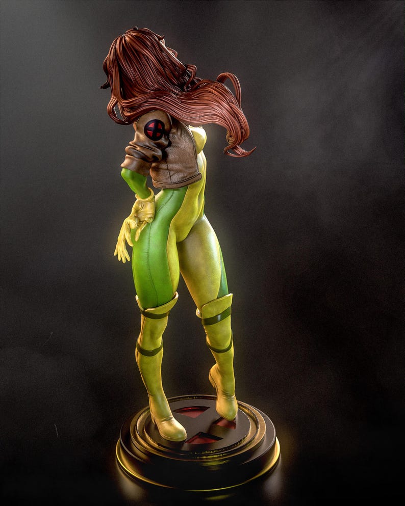 May include: A detailed figurine of Rogue from the X-Men. The statue features a green and yellow bodysuit, a brown jacket with an X-Men logo, and long auburn hair. The figure stands on a round base with a red X symbol.
