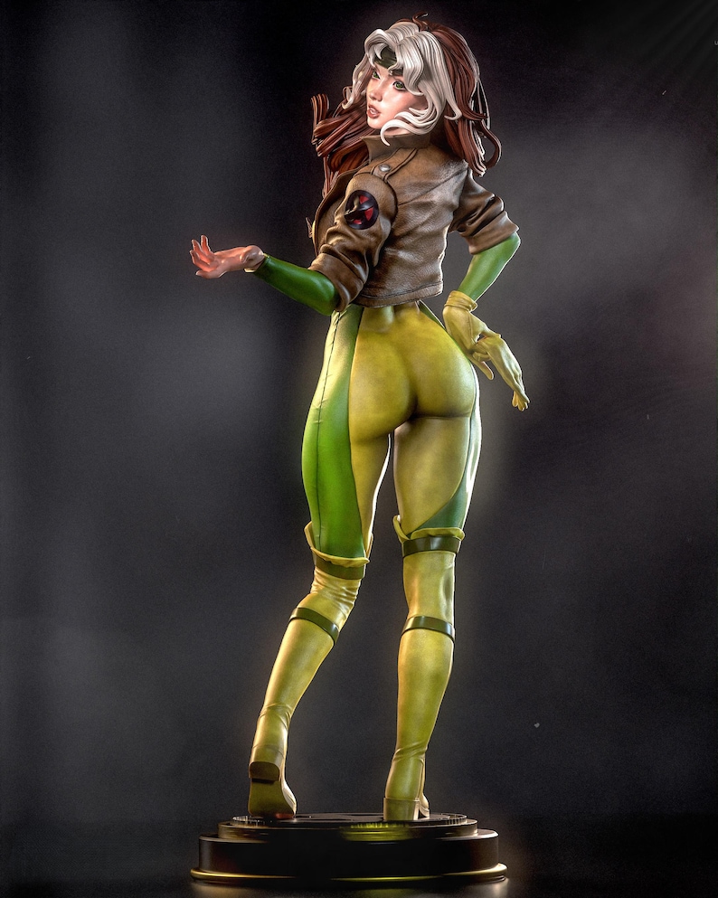 May include: A detailed figurine of a female character in a brown jacket, green gloves, and yellow and green jumpsuit. The figure has brown and white hair and is posed with one arm extended. The figure is standing on a black base.