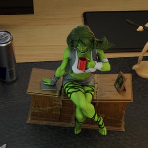 May include: A green She-Hulk figurine seated on a wooden desk, holding a red mug. She wears a grey vest, white top, and a short skirt. Her legs are adorned with green stripes. A framed picture and a can are also visible.