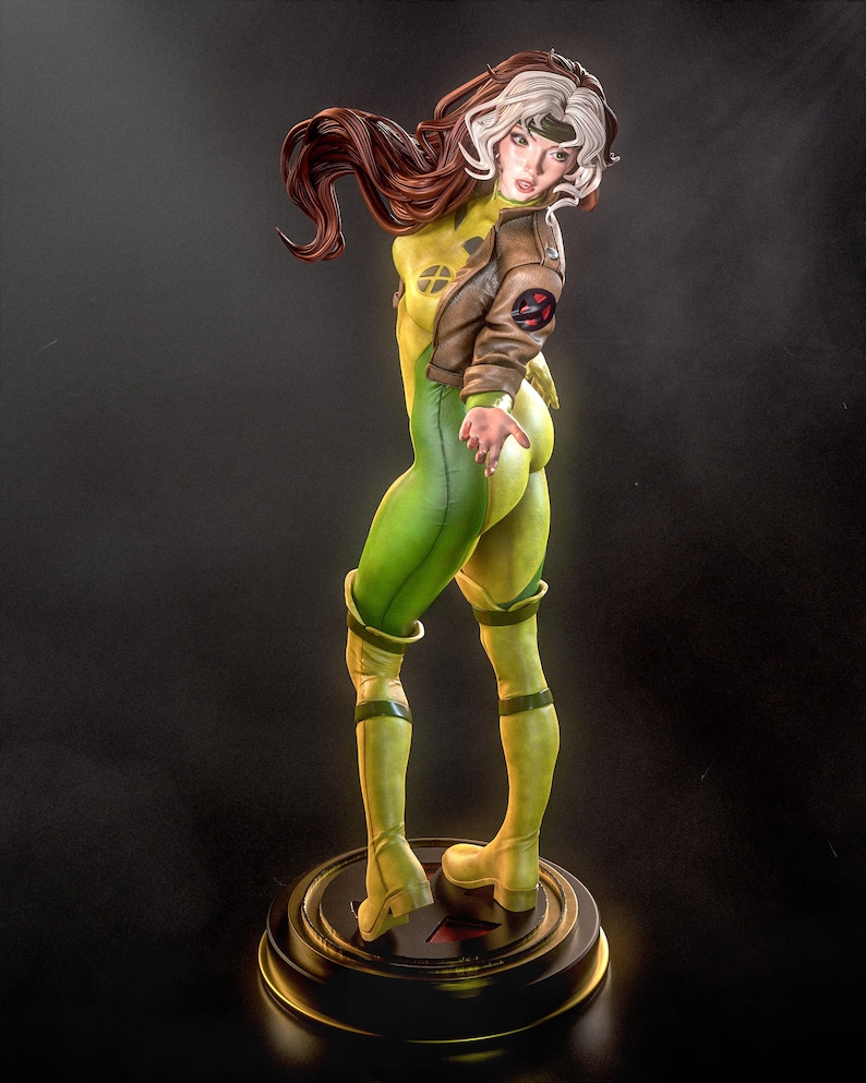 May include: A detailed figurine of a female character in a yellow and green bodysuit, brown jacket, and white-streaked brown hair. The figure is posed on a round base with a gold trim, showcasing a dynamic stance. The character's costume features a distinctive X-Men logo.