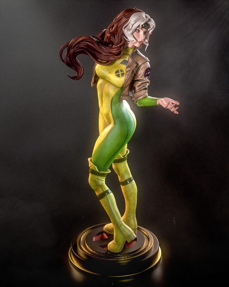 May include: A detailed figurine of Rogue from the X-Men. The statue features Rogue in a dynamic pose, wearing a yellow and green bodysuit, a brown jacket, and boots. Her hair is a mix of brown and white. The figurine is on a round base.