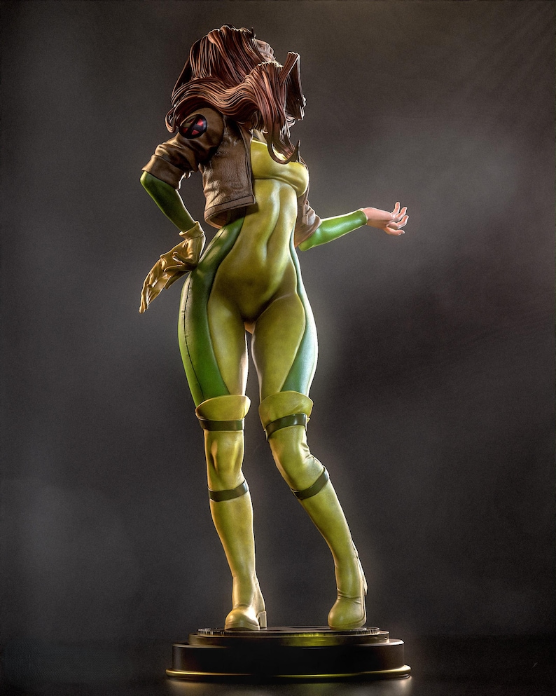 May include: A detailed figurine of a character in a green and yellow bodysuit, brown jacket, and brown hair. The figure is posed on a black base, with one arm extended. The figure has a dynamic pose, with a focus on the character's form and costume.