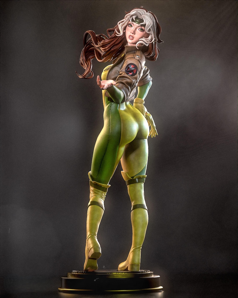 May include: A detailed figurine of a female character in a green and yellow jumpsuit, brown jacket, and boots. The figure has brown and white hair and is posed with one arm extended. The base is black and circular. The overall theme is comic book or superhero.