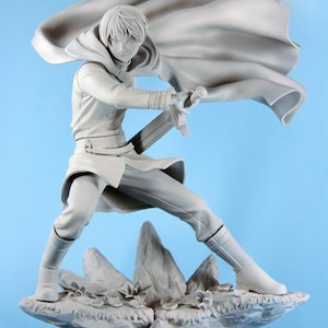 May include: A gray figurine of a person in a dynamic pose, holding a sword. The figure is wearing a long coat with a flowing cape, boots, and pants. The figure is standing on a rocky base with small plants.