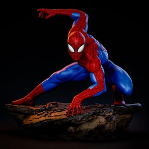 May include: A detailed figurine of Spider-Man in a dynamic pose, poised on a rocky base. The superhero is clad in his iconic red and blue suit, with white eye lenses. The figure is set against a dark background, highlighting the vibrant colors.