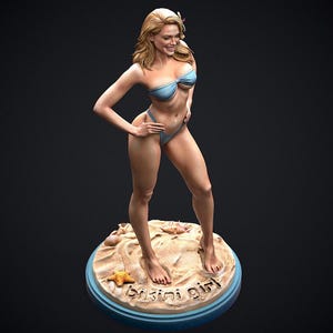 May include: A figurine of a woman in a light blue bikini, standing on a sandy beach base with seashells and a starfish. The base has the words "Bikini Girl" inscribed. The woman has blonde hair and is smiling.