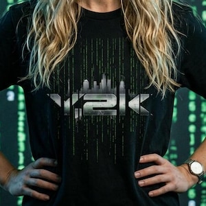 May include: A person wearing a black t-shirt with the text "Y2K" in a silver and green design. The background features a green digital rain pattern. They have long blonde hair and are wearing a watch.