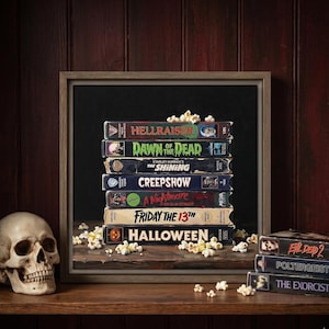 Może przedstawiać: Oprawiony wydruk przedstawiający stos siedmiu klasycznych kaset VHS z horrorami, w tym Hellraiser, Dawn of the Dead, The Shining, Creepshow, A Nightmare on Elm Street, Friday the 13th i Halloween, w otoczeniu rozsypanego popcornu.