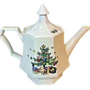 May include: White ceramic teapot with a Christmas tree design. The teapot features a hexagonal body, a curved handle, and a long spout. The Christmas tree is decorated with ornaments and surrounded by gifts.