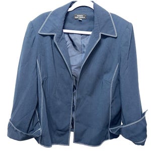 Könnte beinhalten: Ein marineblauer Blazer mit weißen Ziernähten. Die Jacke hat einen Reverskragen, eine offene Front und umgeschlagene Manschetten. Das Etikett lautet "GIORGIO SANT'ANGELO". Der Blazer hängt an einem weißen Kleiderbügel.