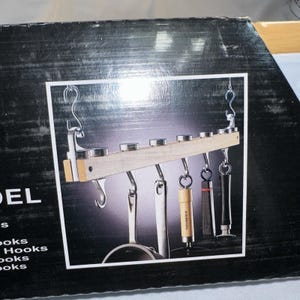 May include: A kitchen utensil rack with a wooden beam and metal hooks. The rack holds various kitchen tools, including a ladle, a corkscrew, and a black and silver item. The rack is suspended by metal hooks.