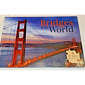 Op de afbeelding: Een doos met vier puzzels van 96 stukjes met afbeeldingen van bruggen van over de hele wereld. De doos heeft een foto van de Golden Gate Bridge bij zonsondergang, met de titel "Bridges of the World".