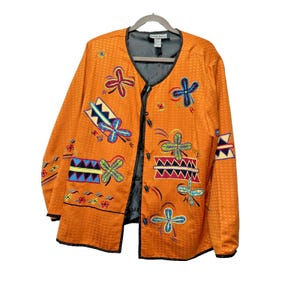 May include: An orange jacket with colorful embroidered floral and geometric designs. The jacket has a textured pattern and black trim. The jacket is open, revealing a gray lining and a black button closure.