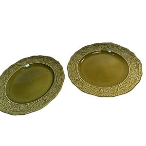 Puede incluir: Dos platos de cerámica verde oliva con patrones florales y de hojas en relieve alrededor de los bordes. Uno es ovalado, el otro redondo con borde festoneado. Los platos tienen un acabado brillante.