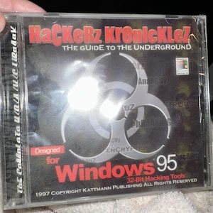 Könnte beinhalten: Eine transparente CD-Hülle aus Kunststoff mit einer Disc namens HaCKeRz KRoNicKLez: The Guide to the Underground. Das Cover zeigt ein großes silbernes Biohazard-Symbol, roten Text und das Windows 95-Logo sowie den Aufdruck 32-bit Hacking Tools.
