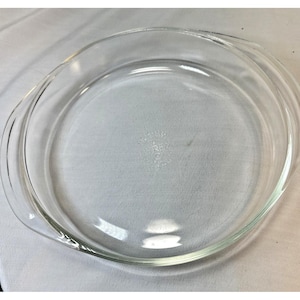 Puede incluir: Un molde para tarta redondo y transparente de Pyrex, con un borde ligeramente elevado y dos asas curvas. El plato de vidrio es transparente, lo que permite una vista completa del contenido. El plato está diseñado para hornear y servir tartas.