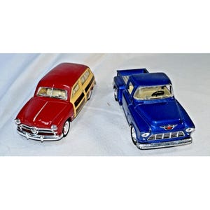 Puede incluir: Dos coches de juguete antiguos: un familiar rojo y beige y una camioneta azul. El familiar tiene una carrocería roja con paneles de madera beige. La camioneta azul tiene una parrilla cromada y un emblema rojo.