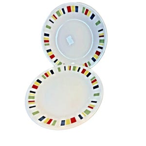 Può includere: Due piatti in ceramica bianca con un bordo colorato di rettangoli rossi, gialli, verdi e blu. I piatti sono rotondi con un bordo leggermente rialzato. I piatti sono puliti e sembrano inutilizzati.